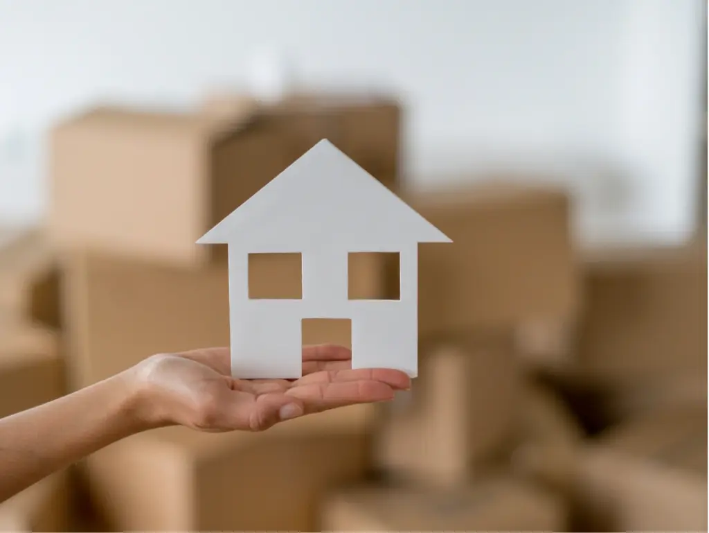 Ausgestreckte Hand mit einem Haus aus Pappe auf der Handfläche als Symbol für die Kosten eines Privat- und Seniorenumzugs.