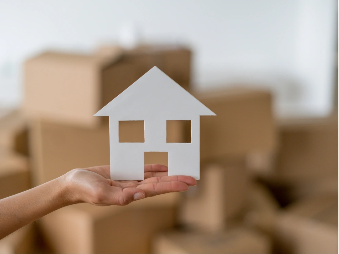 Ausgestreckte Hand mit einem Haus aus Pappe auf der Handfläche als Symbol für die Kosten eines Seniorenumzugs.